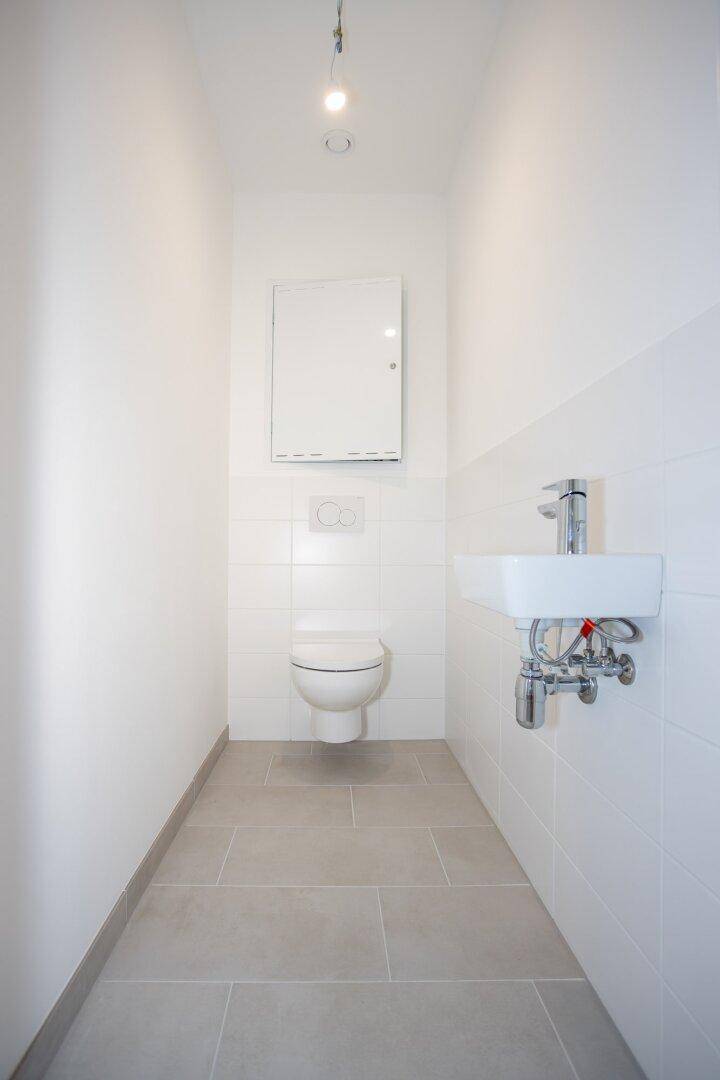 Schmale Gästetoilette mit wandhängendem WC und kleinem Waschbecken.