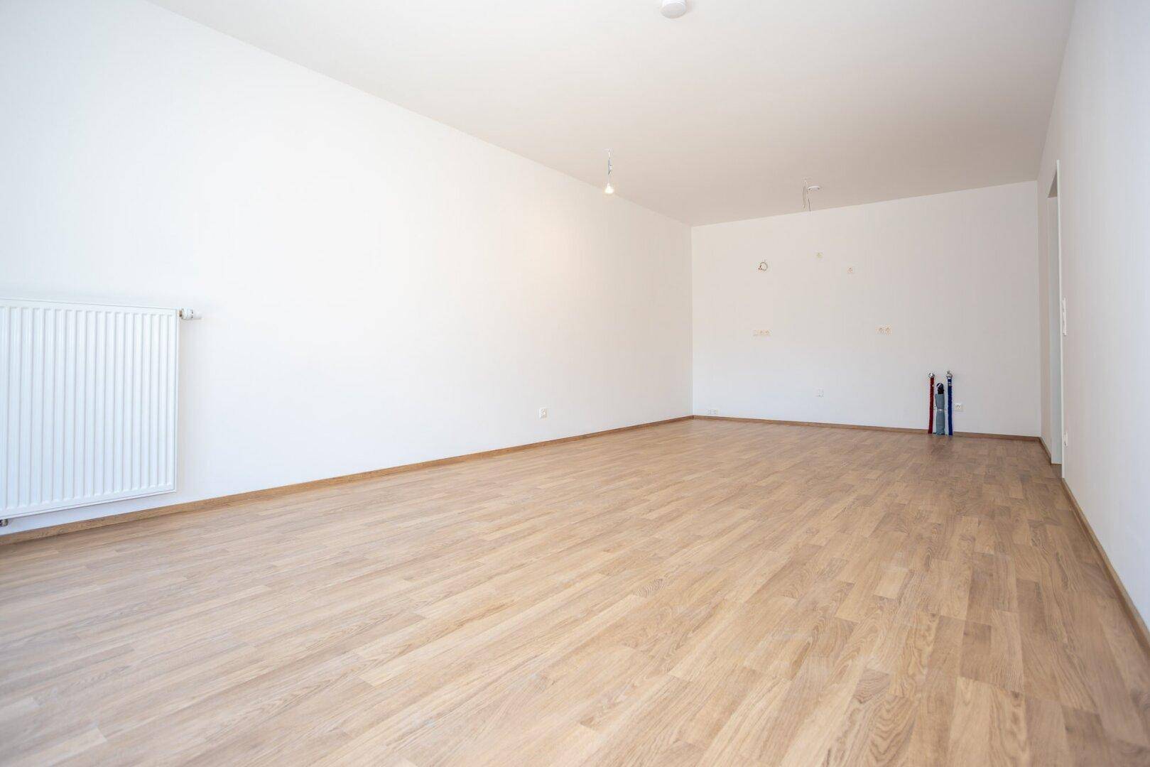 Leerer Raum mit Laminatboden und Anschlüssen für eine zukünftige Küche.