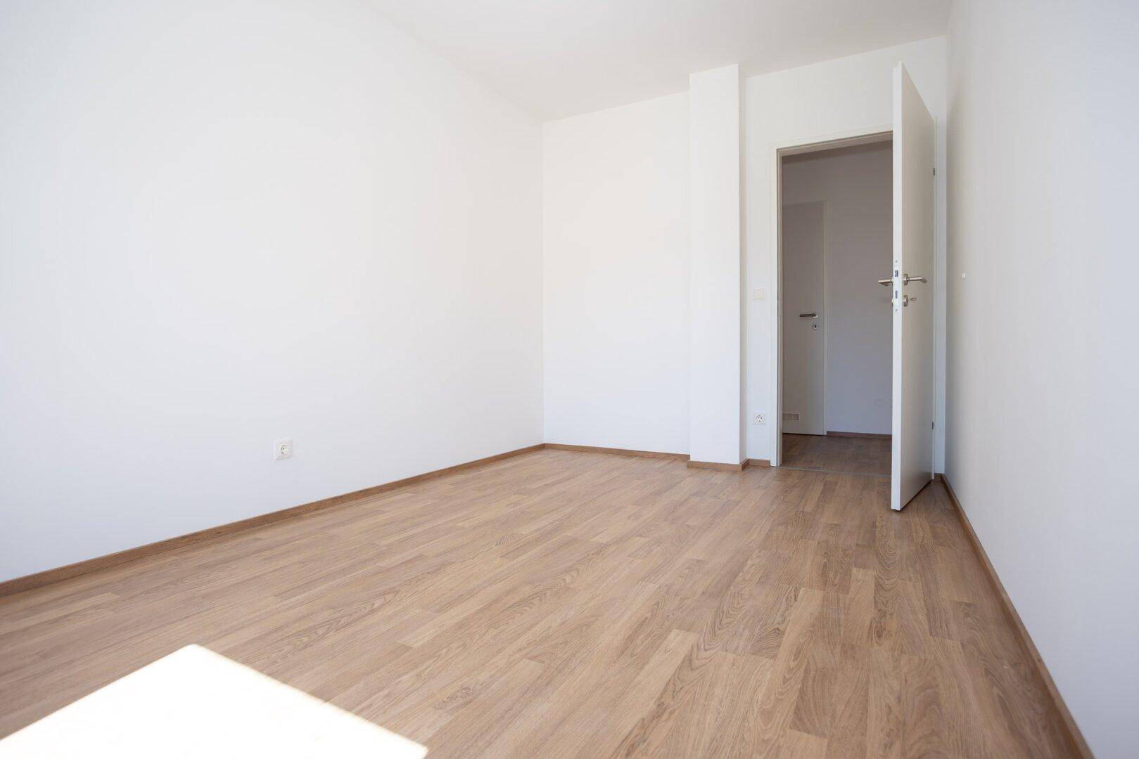 Leeres Zimmer mit Laminatboden und offener Tür, bereit für die individuelle Gestaltung.