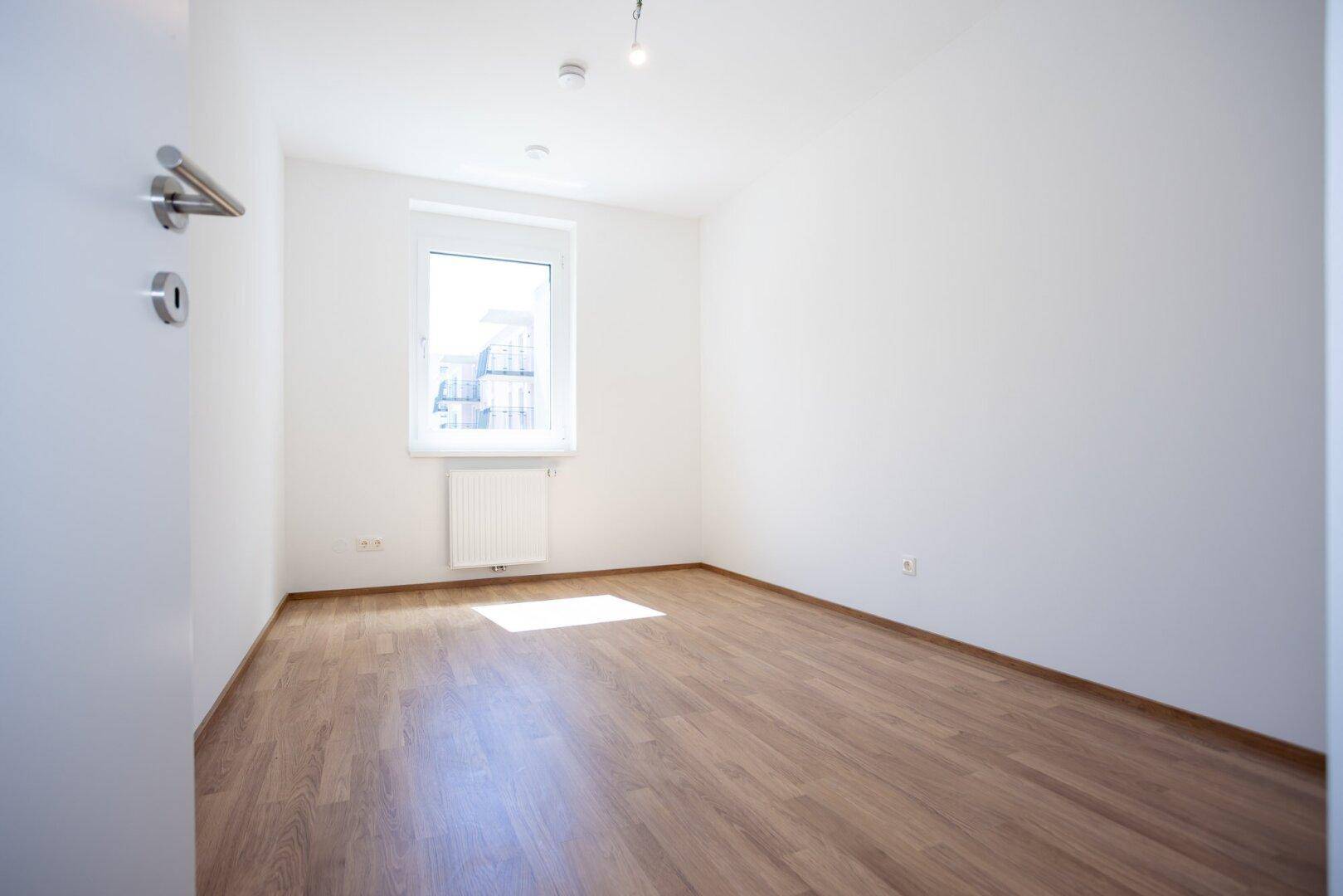 Helles Zimmer mit Laminatboden und Fenster, das viel Tageslicht hereinlässt.