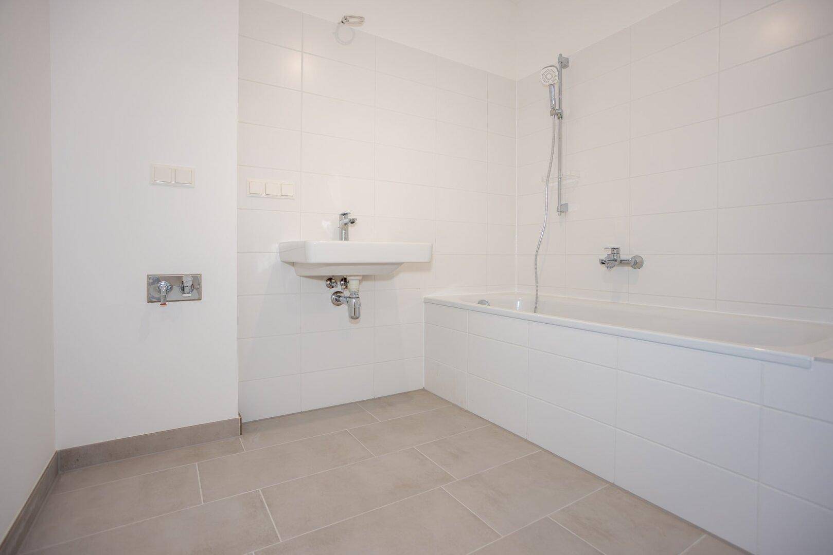 Modernes Badezimmer mit Badewanne, Waschbecken und weißen Fliesen an den Wänden.