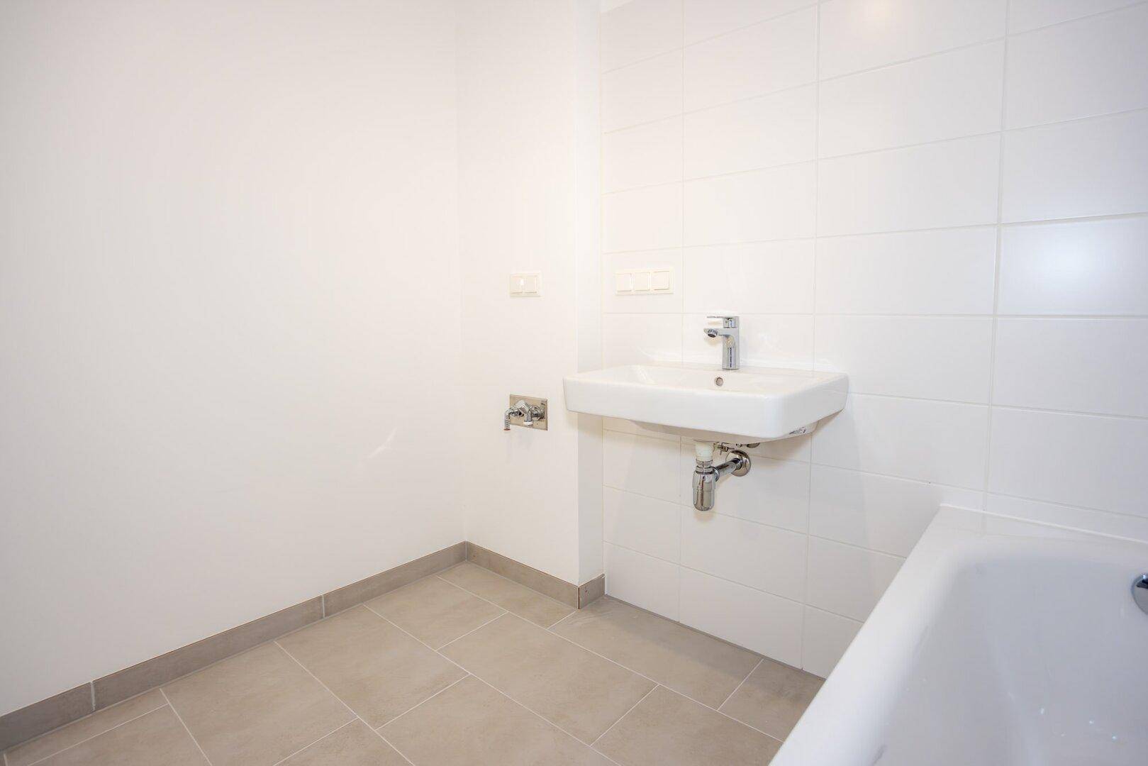 Helles Badezimmer mit weißem Waschbecken und Badewanne, ausgestattet mit modernen Armaturen.