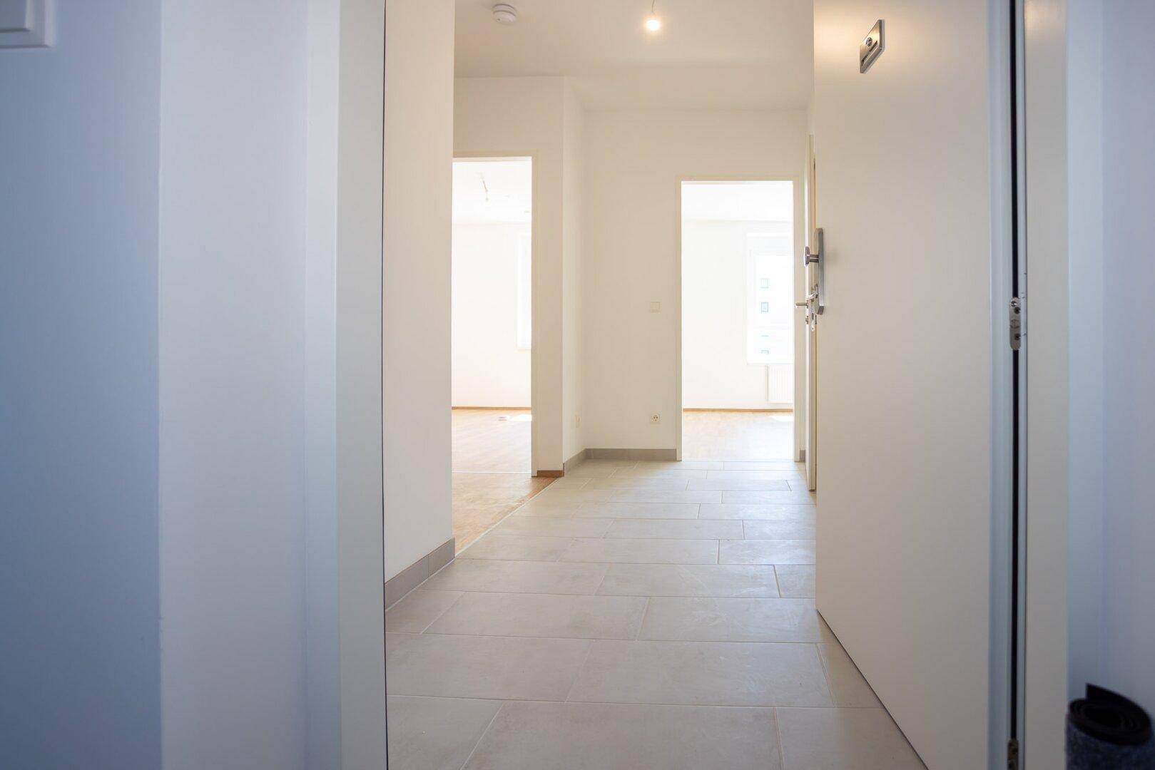 Heller Flur mit Fliesenboden, der zu verschiedenen Räumen der Wohnung führt.