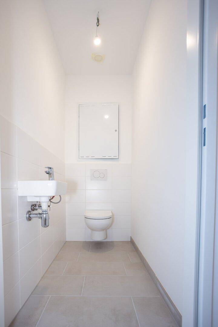 Separates Gäste-WC mit wandhängender Toilette und kleinem Waschbecken, hell gefliest.