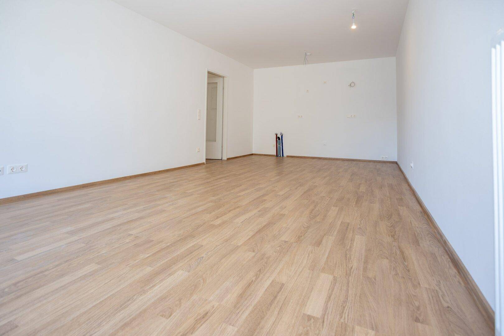 Leerer Raum mit hellem Laminatboden und weißen Wänden, bereit zur individuellen Gestaltung.
