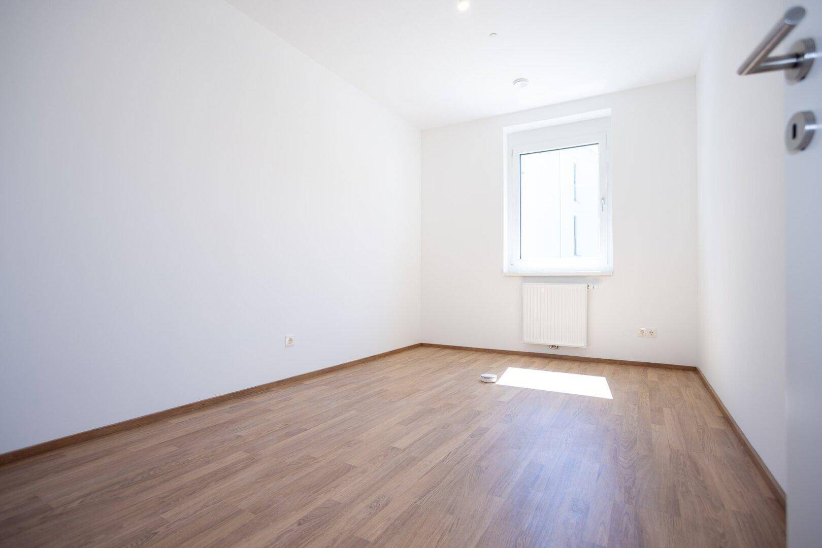 Freundliches Schlafzimmer mit Laminatboden und einem Fenster, das den Raum gut belichtet.