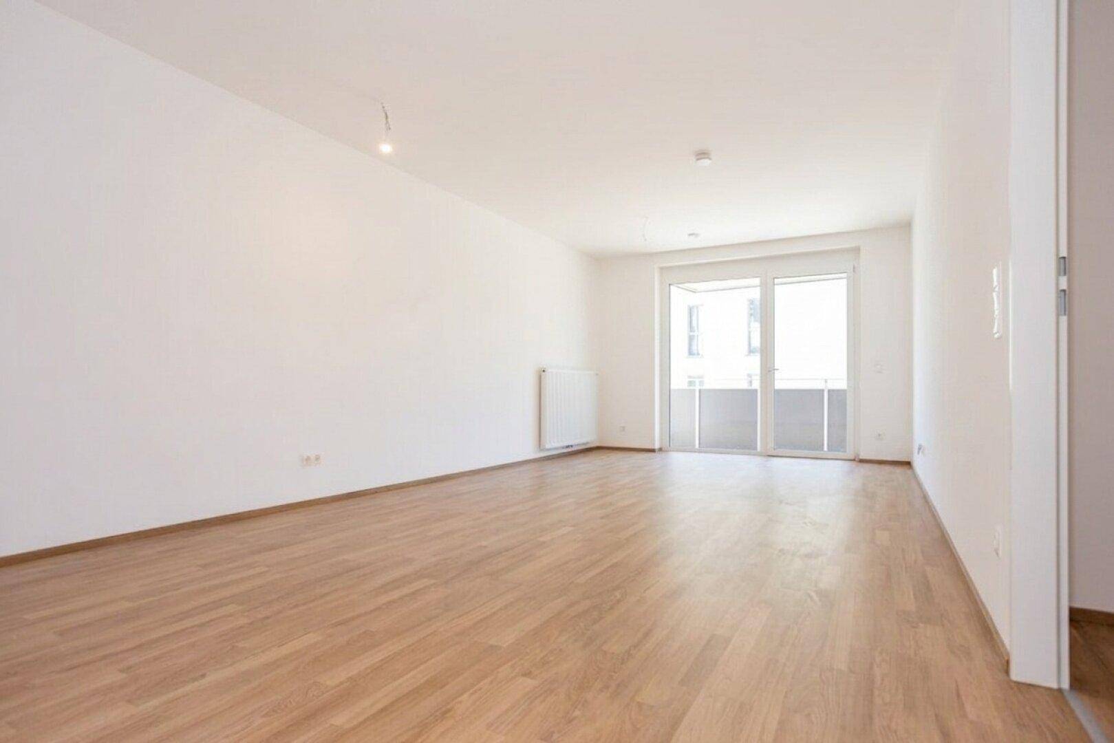 Geräumiges, unmöbliertes Wohnzimmer mit Laminatboden und großen Fenstern für viel Licht.