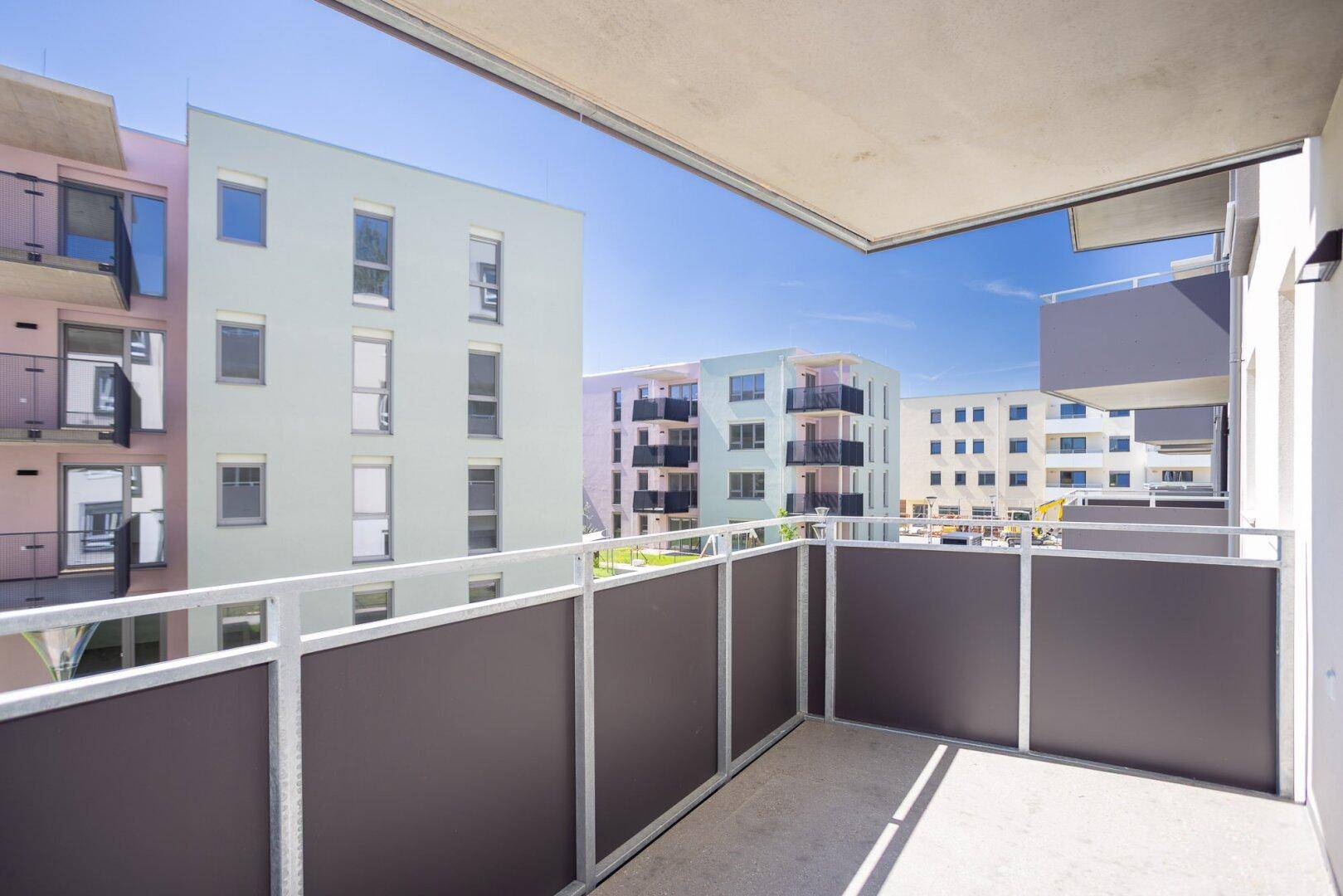 Heller Balkon mit Blick auf moderne Wohngebäude und blauen Himmel an einem sonnigen Tag.