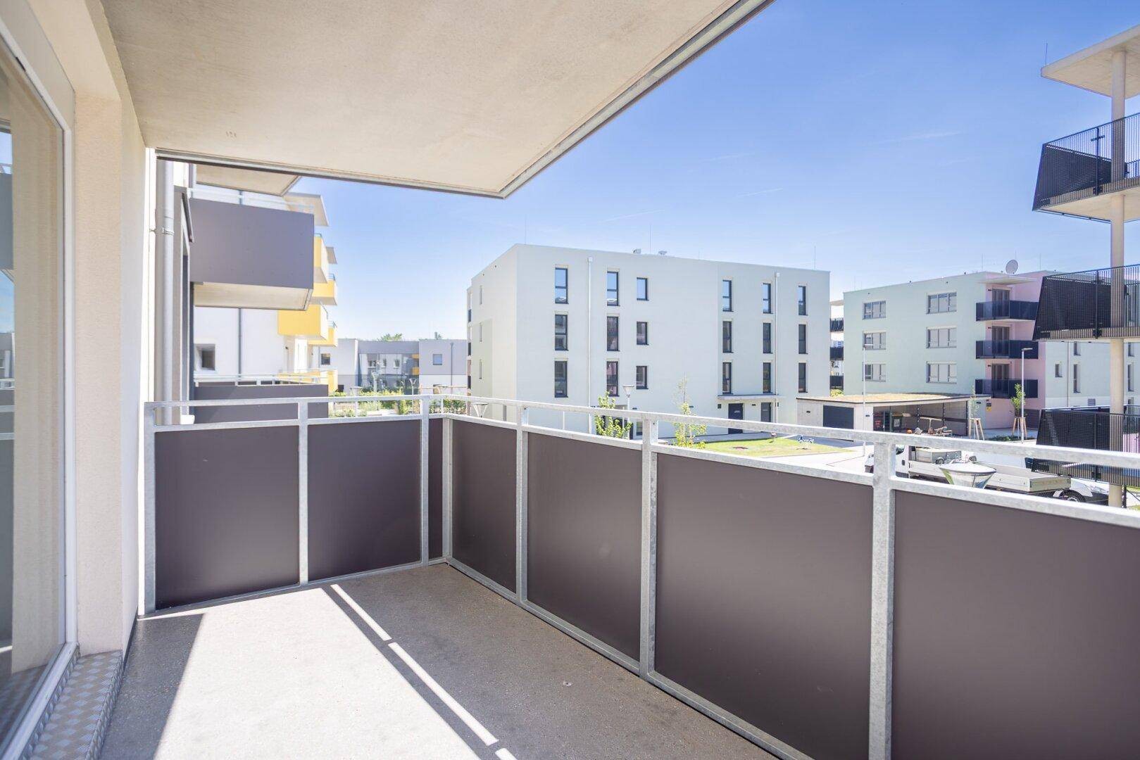 Geräumiger Balkon mit Blick auf die umliegenden Neubauten unter blauem Himmel und Sonnenschein.