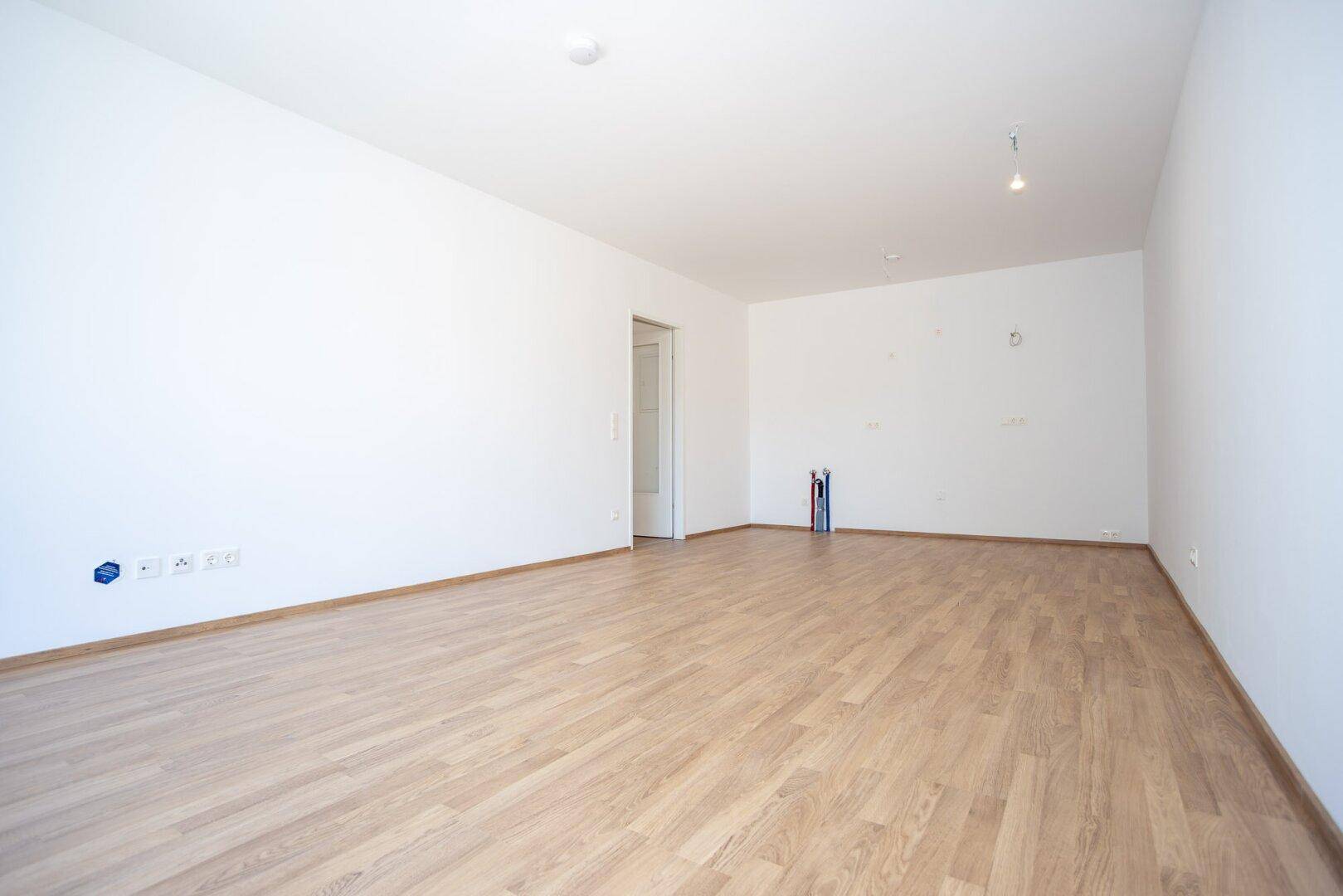 Leerer Raum, vorbereitet für eine Küche, mit Laminatboden und sichtbaren Anschlüssen.