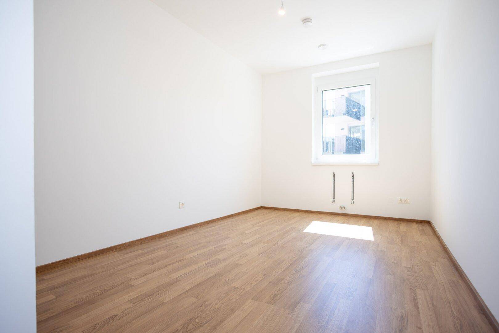 Geräumiges Schlafzimmer mit Laminatboden und einem Fenster, das viel Tageslicht hereinlässt.