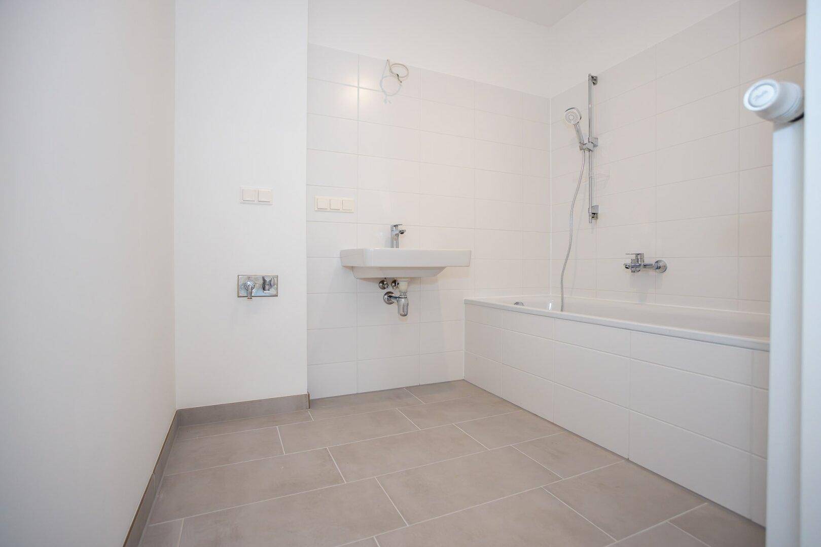Modernes Badezimmer mit weißen Wandfliesen, grauen Bodenfliesen, Badewanne und Waschbecken.