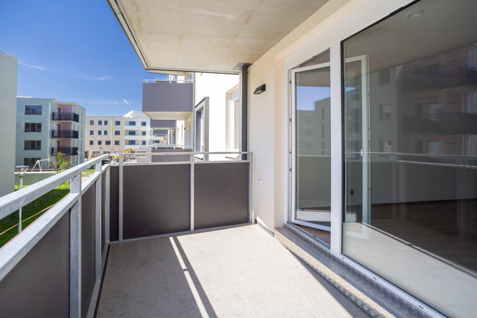 Geräumiger Balkon mit Schiebetür zum Innenbereich und sonnigem Ausblick auf die Umgebung.
