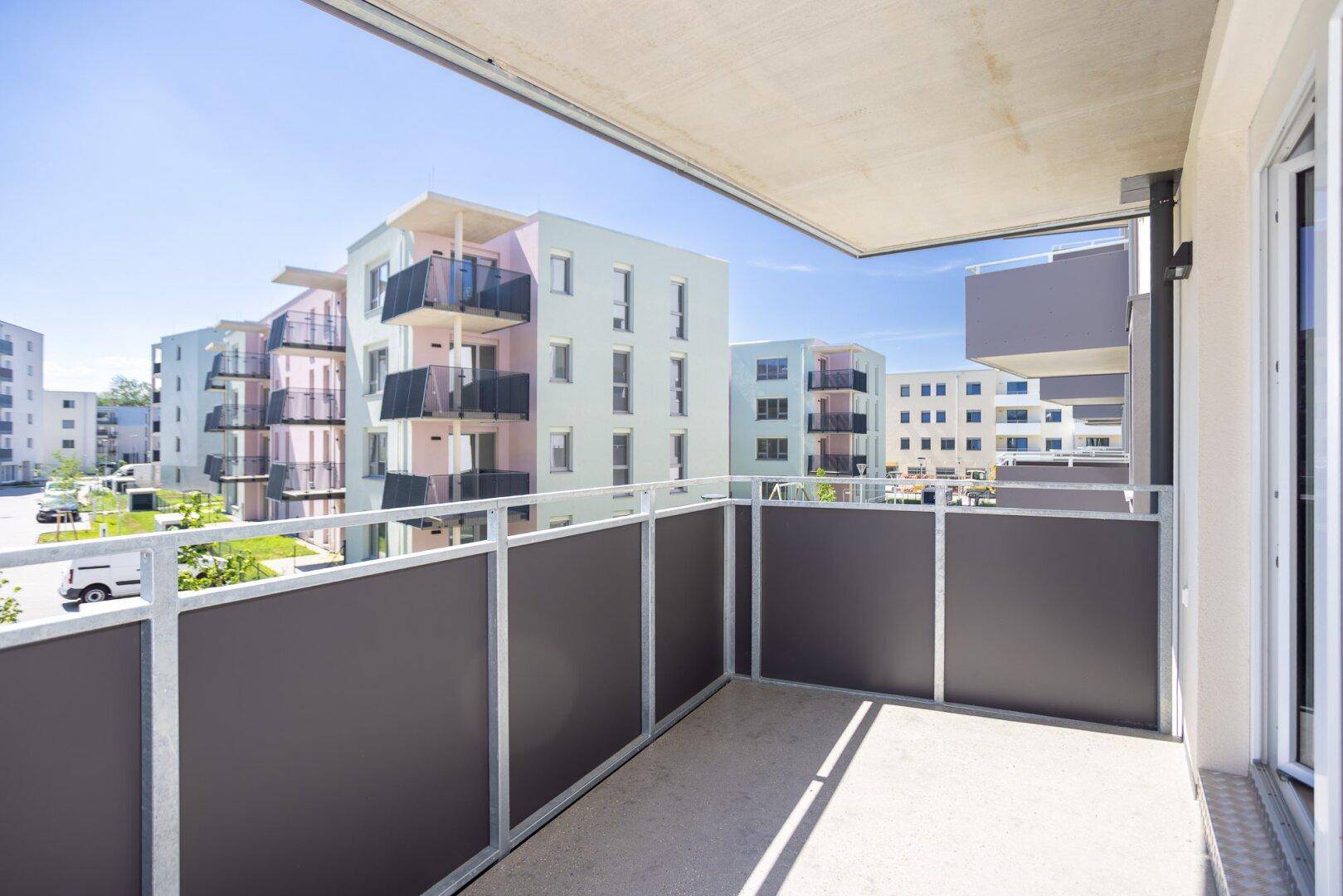 Heller Balkon mit grauen Geländern und Blick auf moderne Wohngebäude unter blauem Himmel.