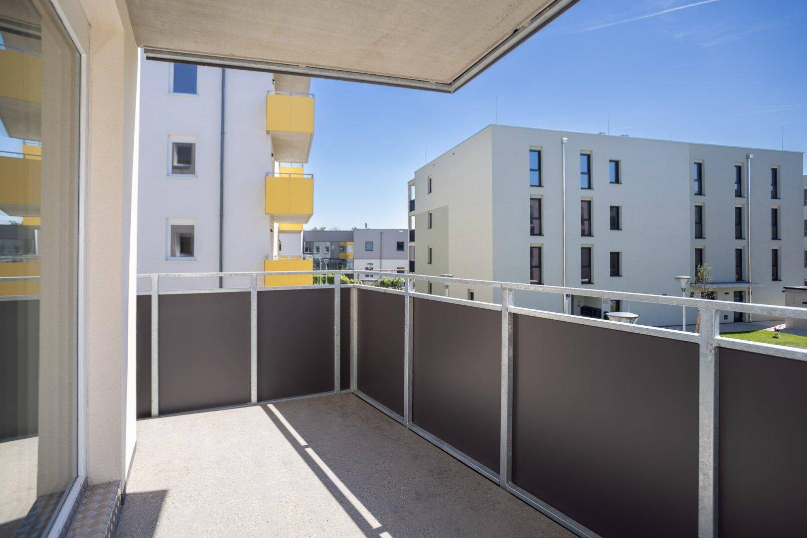 Sonniger Balkon mit Blick auf die umliegenden Neubauten und klarem blauen Himmel.