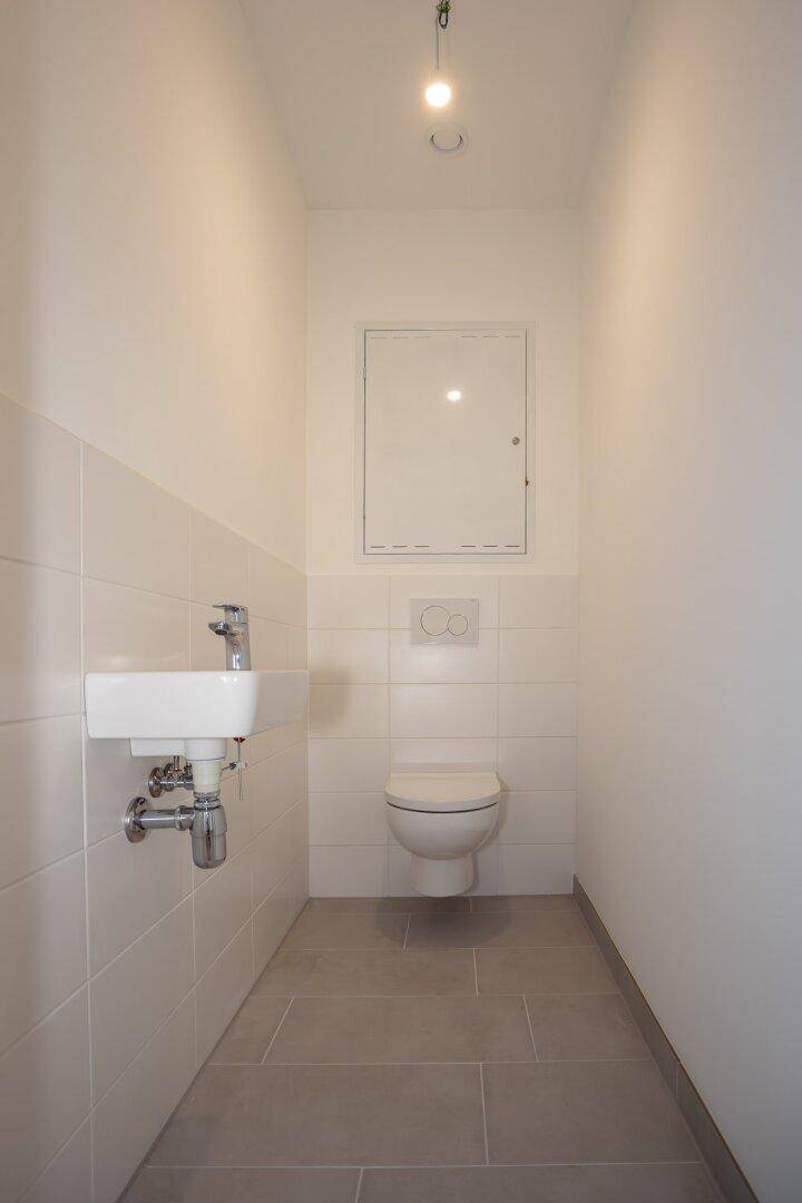 Kleines Gäste-WC mit wandhängender Toilette, kleinem Waschbecken und modernen Fliesen.