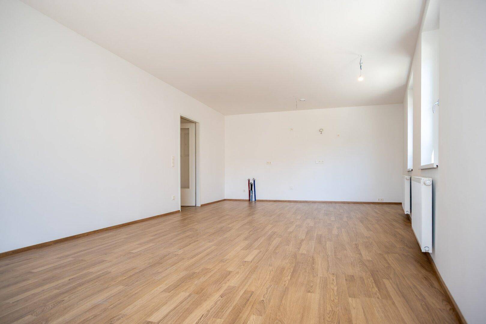 Leeres Zimmer mit Laminatboden, weißen Wänden und einem Türrahmen, bereit zur Einrichtung.