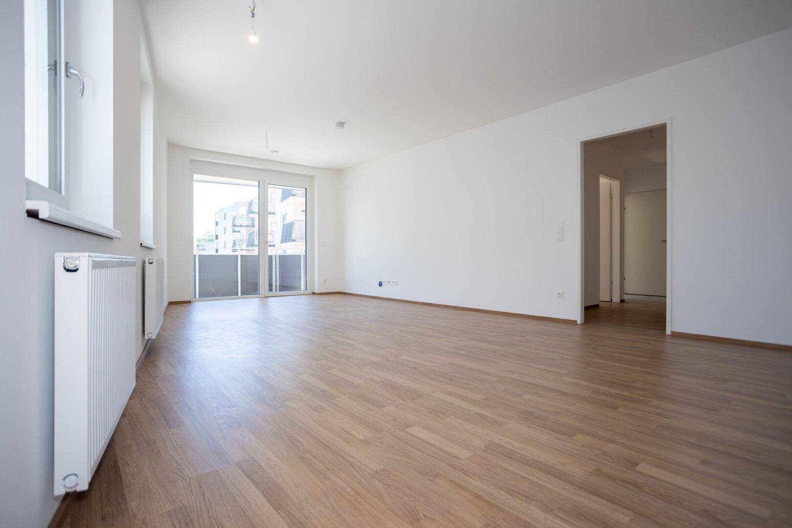 Geräumiges, helles Zimmer mit Laminatboden und Zugang zu einem Flur und Balkon.