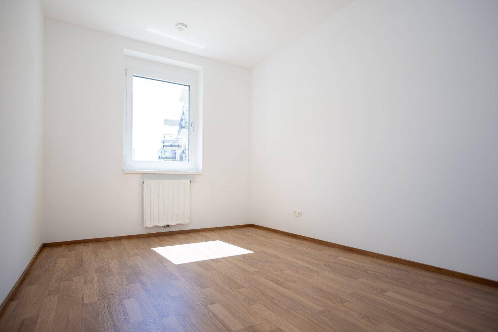 Leeres Schlafzimmer mit Laminatboden, weiß gestrichenen Wänden und einem Fenster.