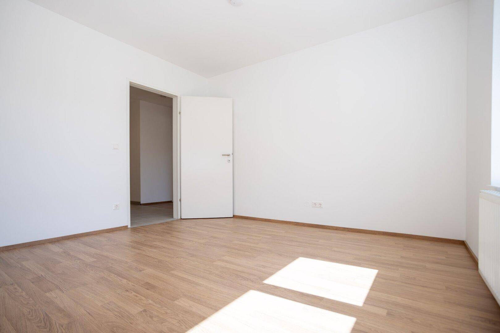 Leeres Schlafzimmer mit Laminatboden und weißer Tür, bereit für individuelle Gestaltung.