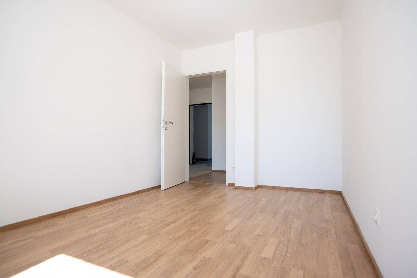 Helles Schlafzimmer mit Laminatboden und offener Tür, bereit zur Einrichtung.