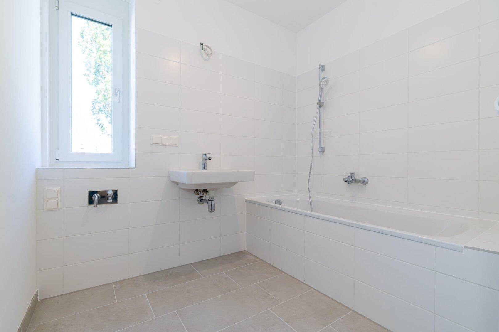 Modernes Badezimmer mit weißen Fliesen, Badewanne, Waschbecken und Fenster für Tageslicht.
