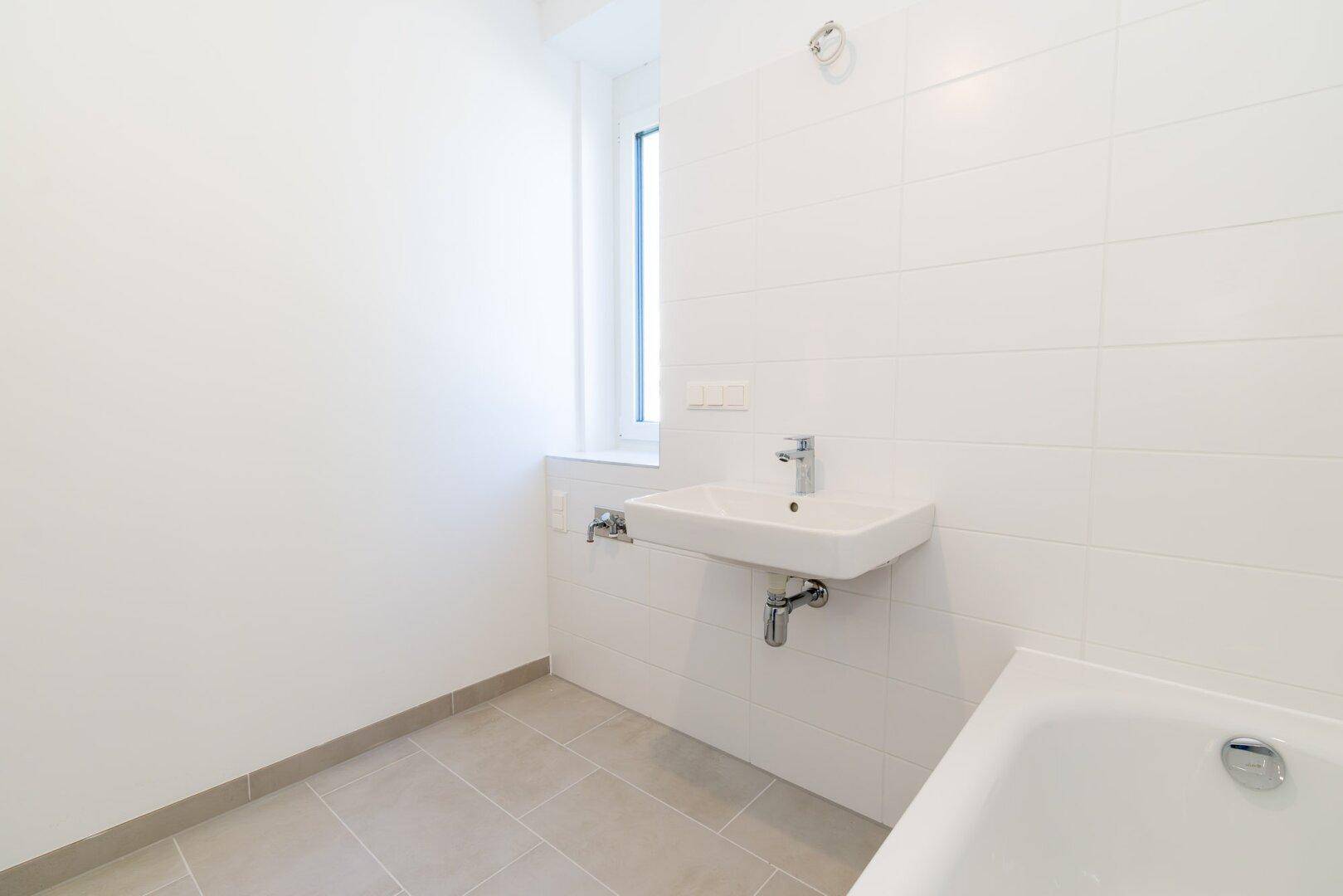 Helles Badezimmer mit weißen Wandfliesen, Badewanne und modernem Waschbecken.