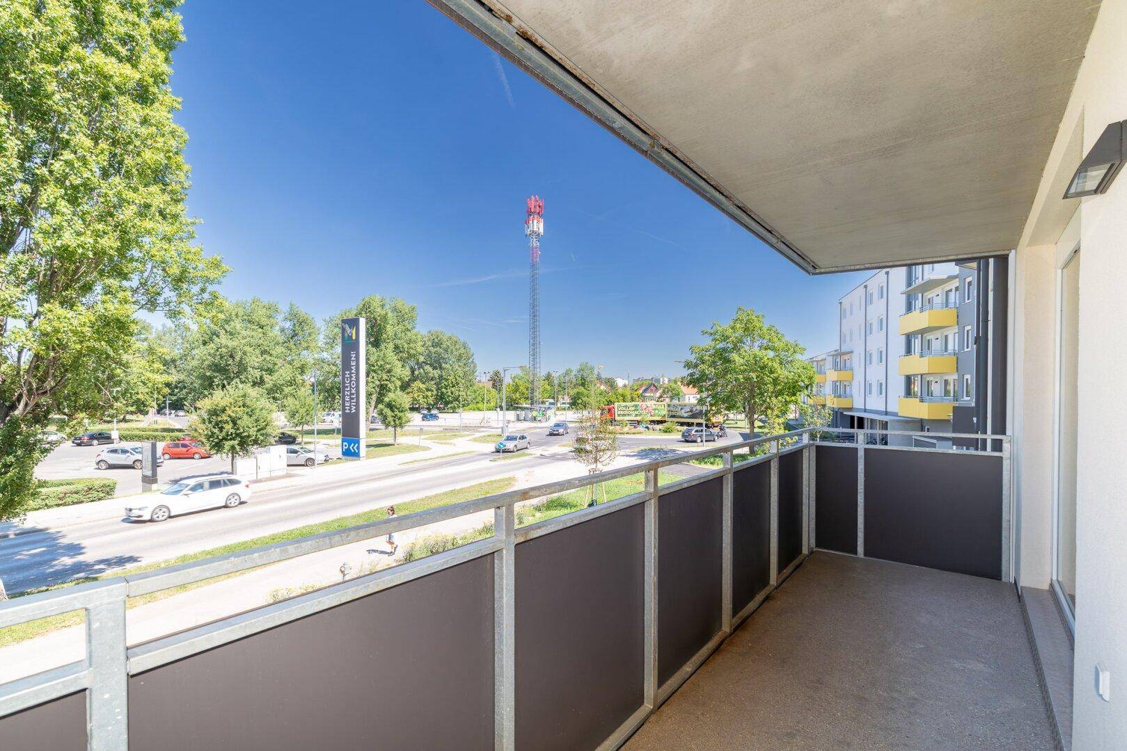 Balkon mit Weitblick über eine Straße, Bäume und einen Mobilfunkmast in der Ferne.