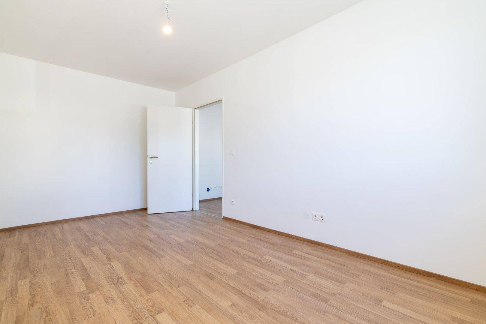Leeres Zimmer mit Laminatboden und weiß gestrichenen Wänden, bereit zum Einrichten.