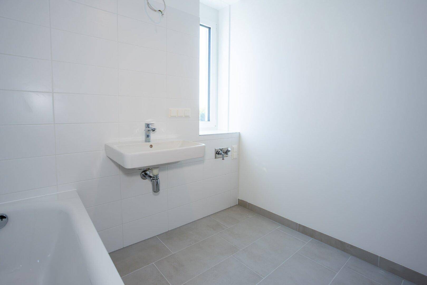 Helles Badezimmer mit Waschbecken, weißen Fliesen und Fenster, das eine angenehme Atmosphäre schafft.