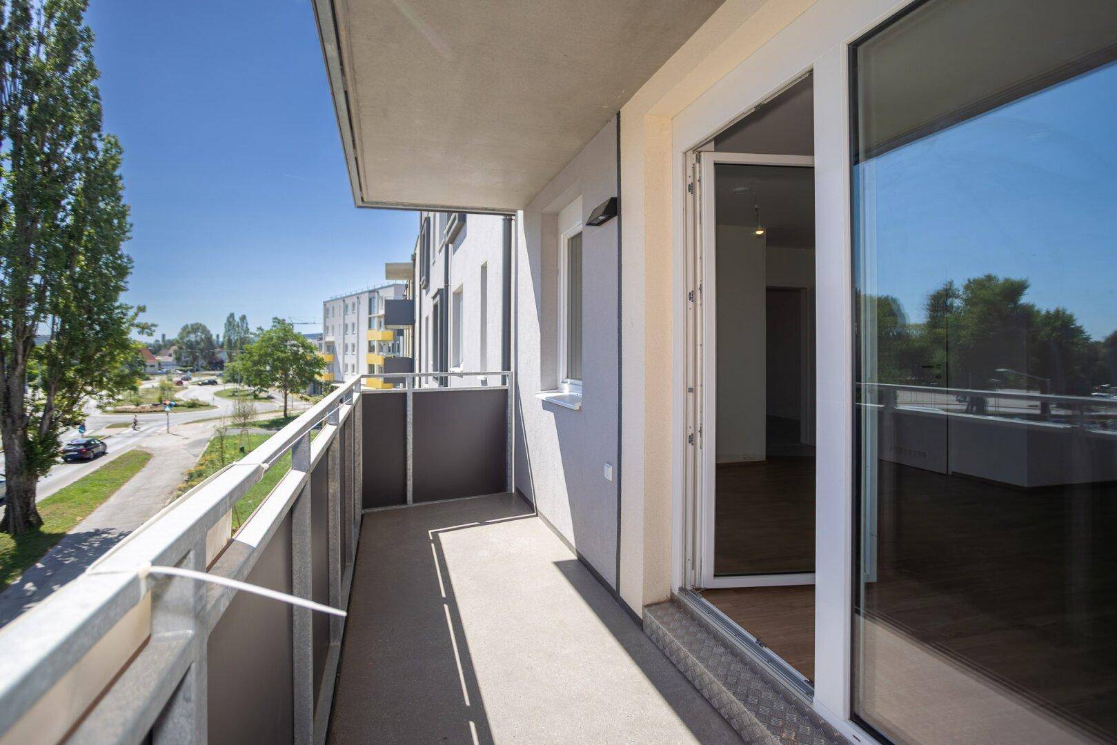 Heller Balkon mit Zugang zum Innenbereich und Blick auf die Umgebung.