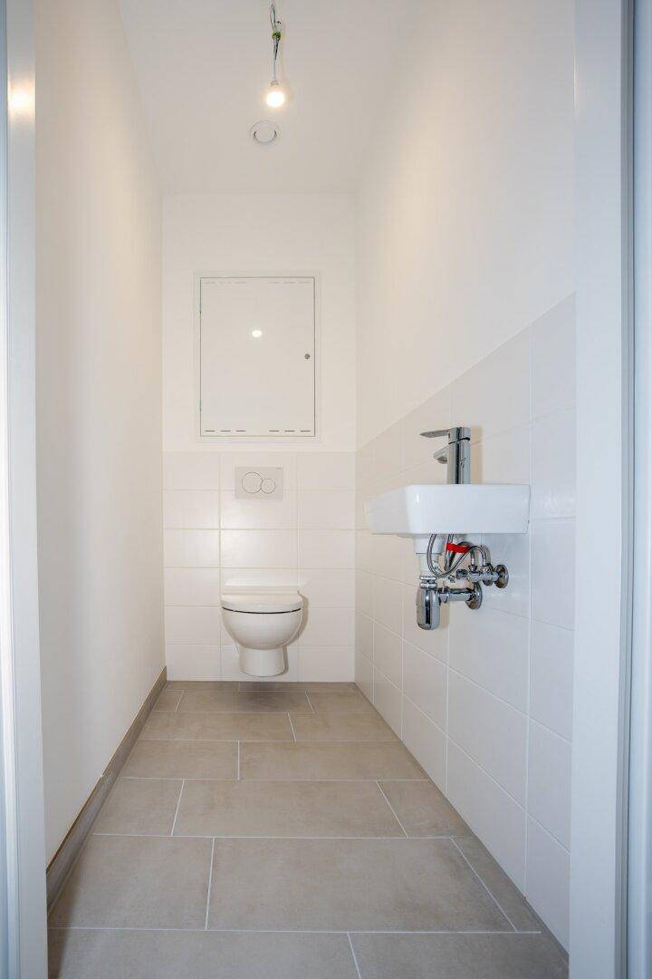 Modernes Gäste-WC mit wandhängender Toilette, kleinem Waschbecken und hellen Fliesen.