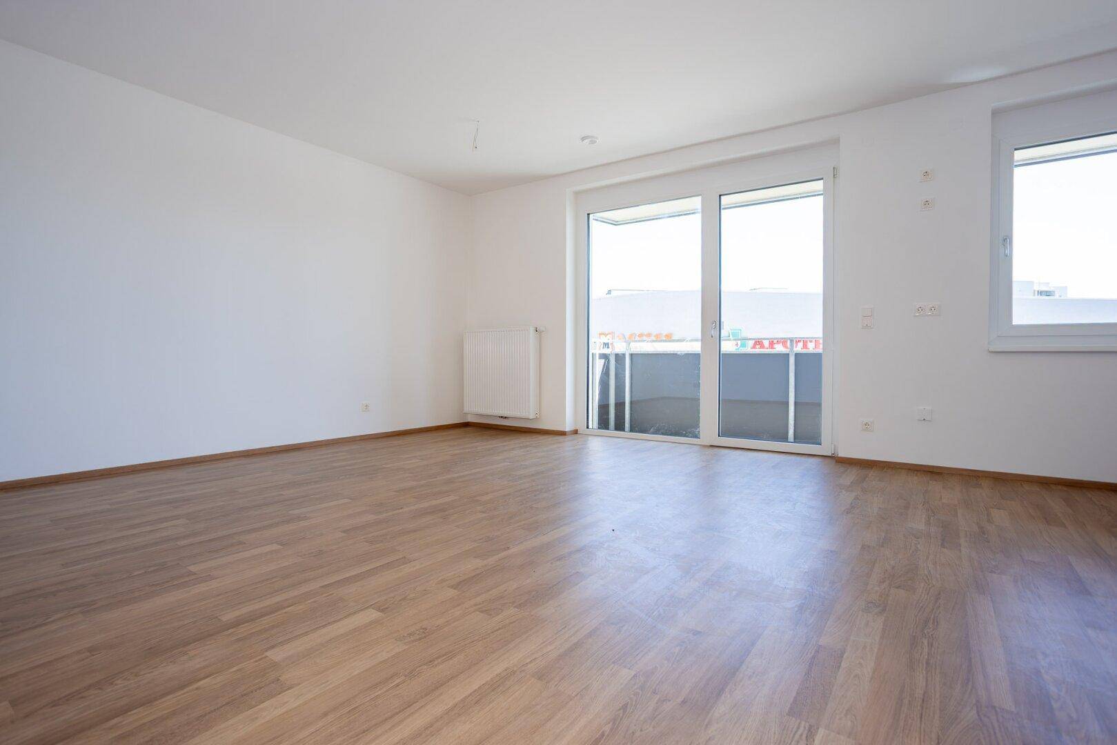 Helles, unmöbliertes Zimmer mit Laminatboden und Schiebetür zum Balkon.