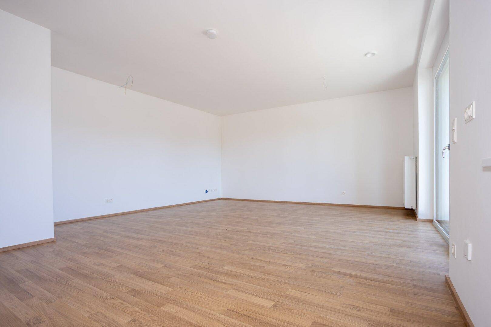 Weitläufiges, leeres Zimmer mit großen Fenstern und hellem Laminatboden, bereit zur Einrichtung.