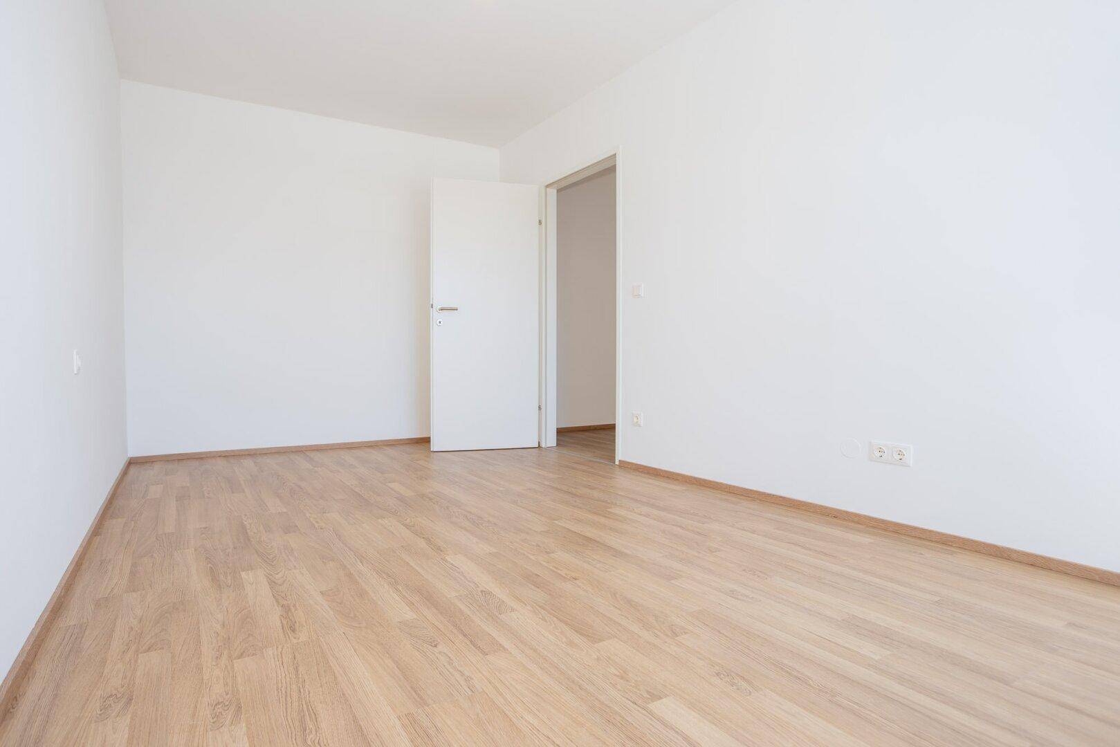 Leeres Zimmer mit Laminatboden und einer offenen Tür, bereit zur individuellen Gestaltung.