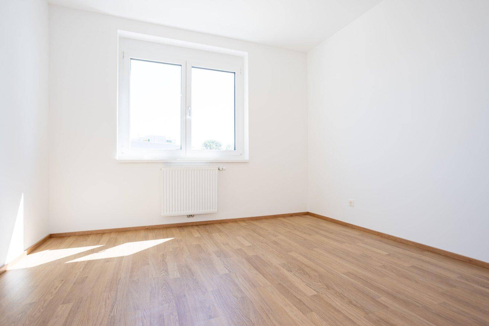Helles Zimmer mit Laminatboden und einem Fenster, das für natürliche Belichtung sorgt.