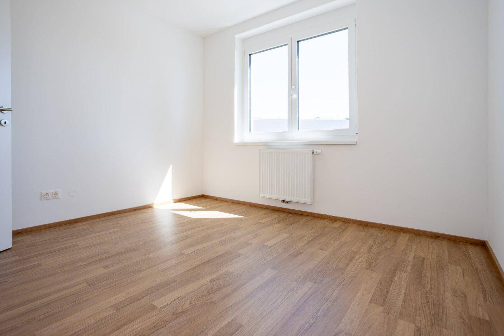 Unmöbliertes Zimmer mit Laminatboden und Fenster, ideal als Schlaf- oder Arbeitszimmer.