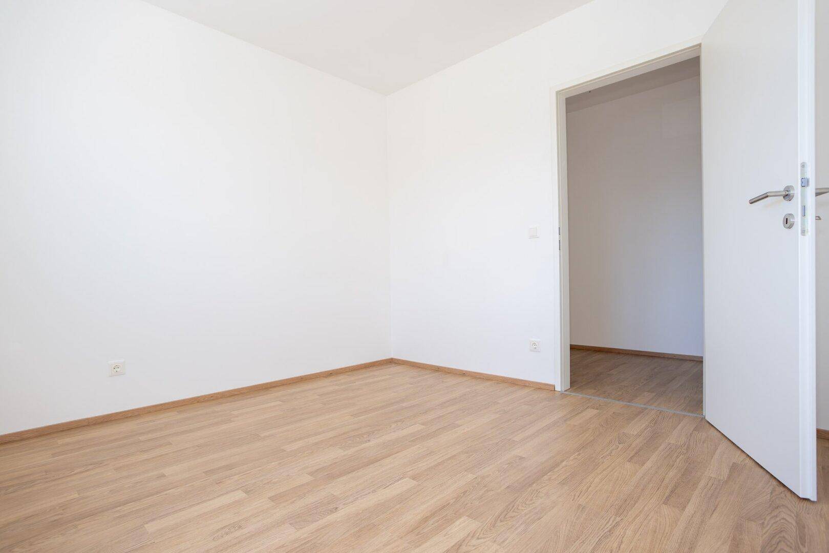 Leeres Zimmer mit Laminatboden und offener Tür, das auf neue Bewohner wartet.