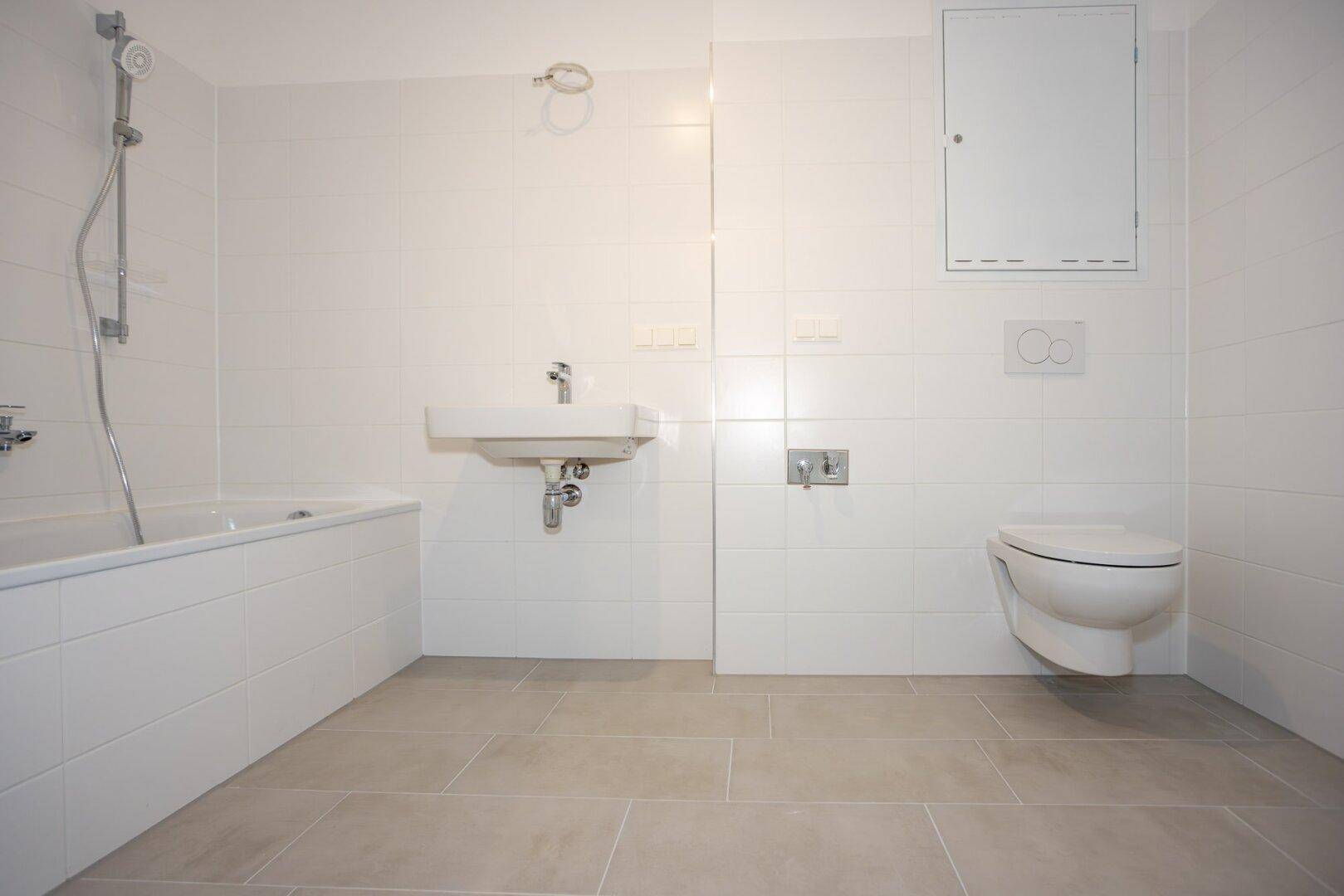 Modernes Badezimmer mit weißen Wandfliesen, heller Bodenfliesen und Badewanne mit Duschfunktion.