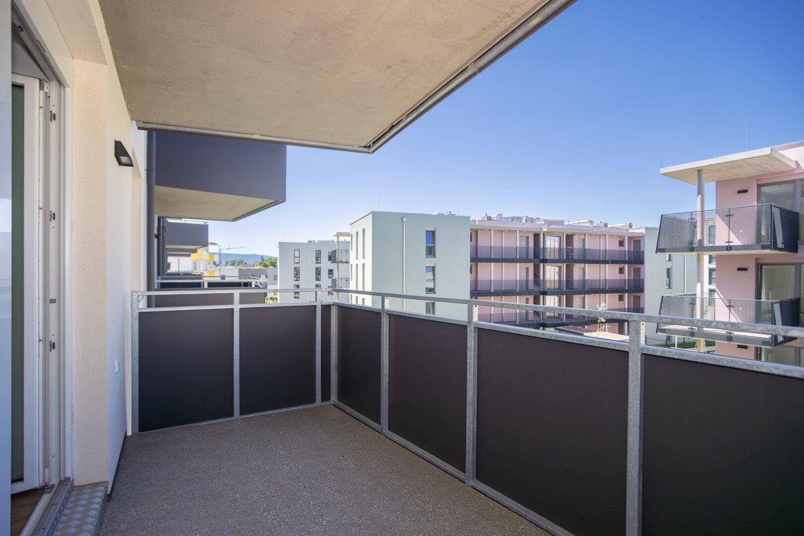 Sonniger Balkon mit Metallgeländer und Ausblick auf die moderne Wohnsiedlung.