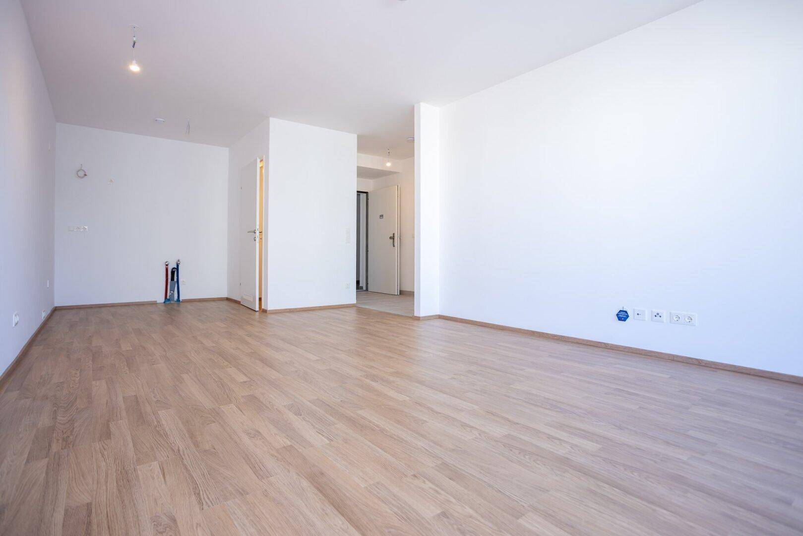 Heller Raum mit Laminatboden und vorbereiteten Anschlüssen für eine moderne Einbauküche.
