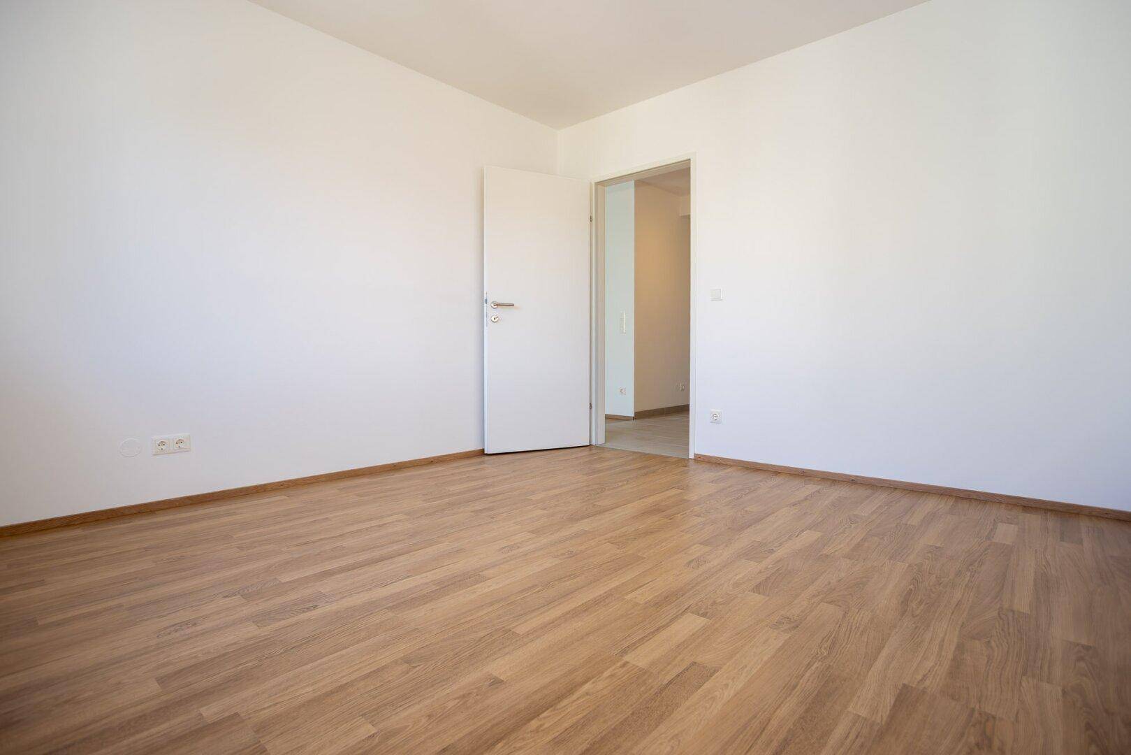 Leeres Zimmer mit Laminatboden und weiß gestrichenen Wänden, bereit zum Einrichten.
