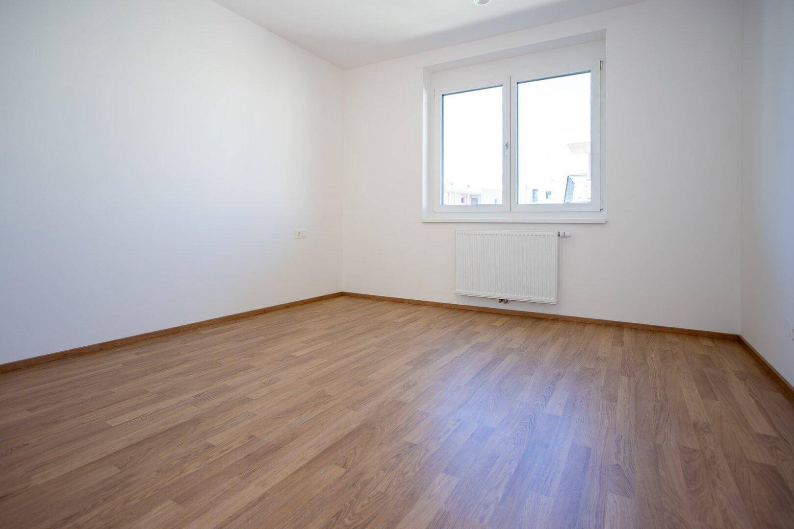 Ruhiges, helles Zimmer mit Laminatboden und großem Fenster, perfekt als Schlaf- oder Arbeitszimmer.