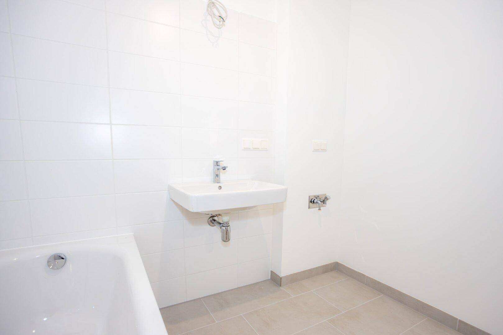 Sauber gefliestes Badezimmer mit Badewanne und modernem Waschbecken, in neuwertigem Zustand.