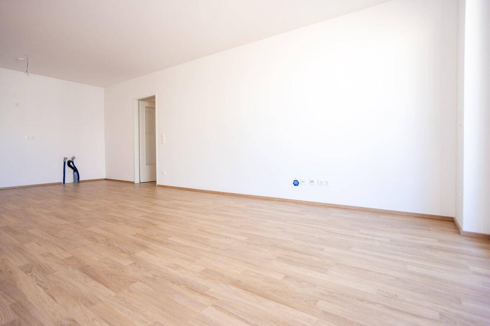 Leerer Raum mit Laminatboden und Anschlüssen für eine zukünftige Einbauküche.