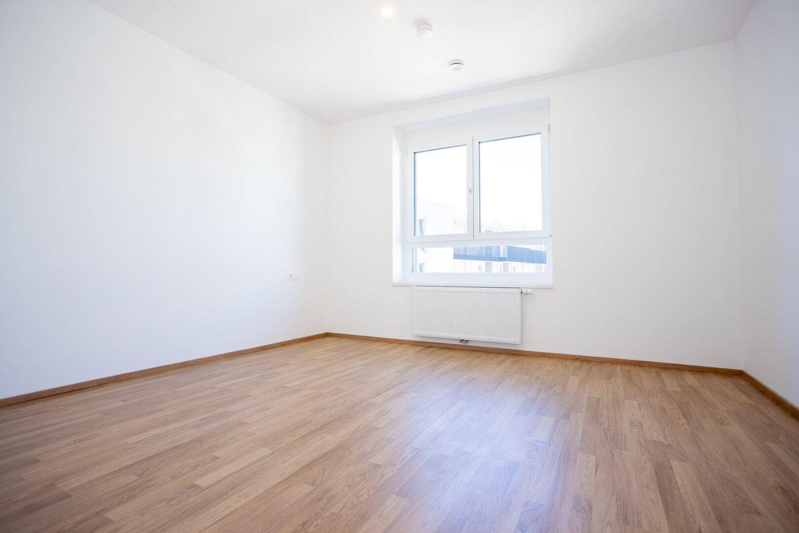 Helles, unmöbliertes Schlafzimmer mit Laminatboden und einem großen Fenster.