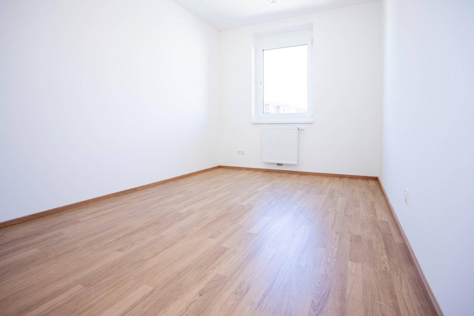 Unmöbliertes Zimmer mit hellem Laminatboden und Fenster, bereit zur individuellen Gestaltung.