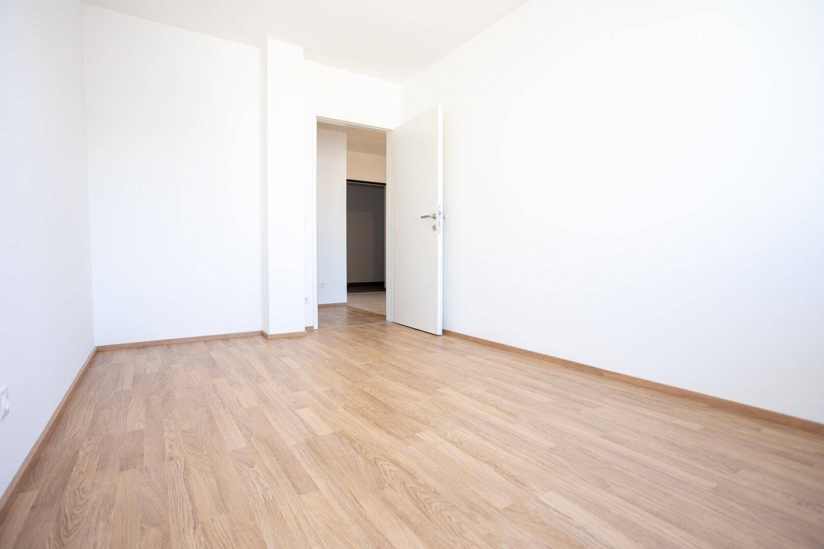 Helles Zimmer mit Laminatboden und offener Tür, bietet vielseitige Nutzungsmöglichkeiten.
