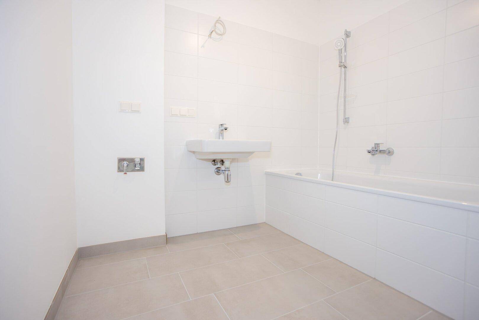 Modernes Badezimmer mit weiß gefliesten Wänden, Badewanne und einem wandhängenden Waschbecken.
