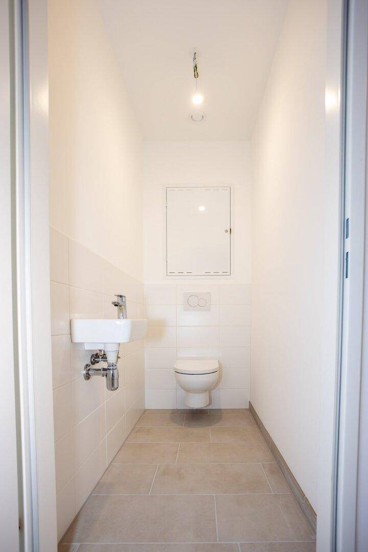 Kleines Gäste-WC mit wandhängender Toilette, kleinem Waschbecken und hellen Fliesen.